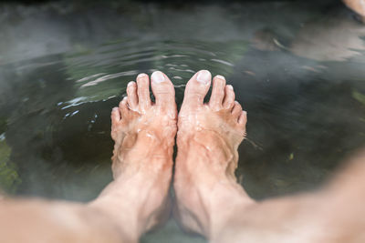 Low section of person relaxing in hot water spring lake