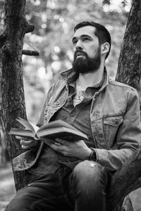 Young man looking away while sitting on tree