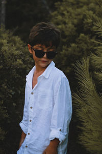 Boy wearing sunglasses standing against plants