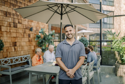 Portrait of smiling male nurse standing with hands clasped at nursing home