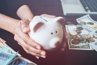 Cropped hands of businesswoman holding piggy bank on table