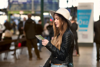 Young woman wearing hat standing against city in background