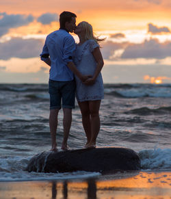 Rear view of couple walking on beach during sunset