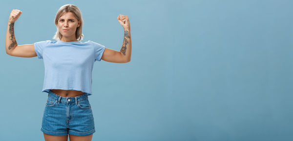 Young woman with arms raised standing against blue background