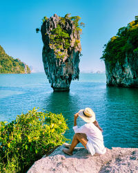 Rear view of woman sitting on rock by sea against sky