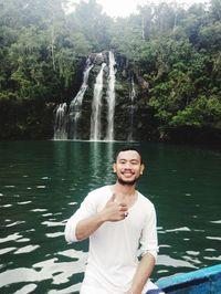 Portrait of smiling man standing against waterfall