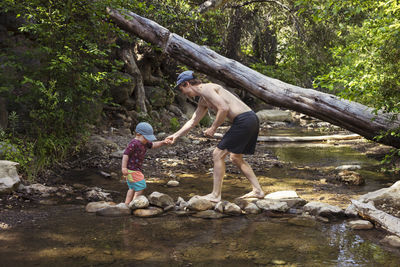 Man helping son to cross stream in forest