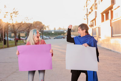 Cheerful female friends laughing while holding posters outdoors