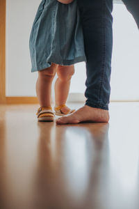 Low section of father and baby girl standing on hardwood floor at home