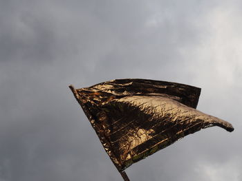 Low angle view of golden flag against cloudy sky