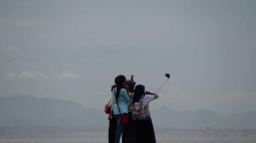 Rear view of people photographing sea against sky