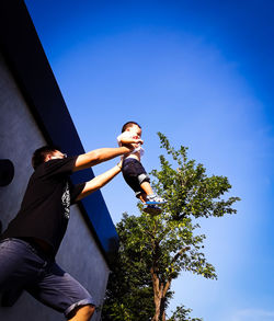 Low angle view of father playing with son against clear blue sky