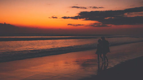 Rear view of woman standing at beach during sunset