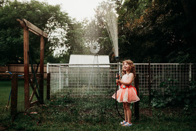 Young girl in dress watering backyard garden with water hose