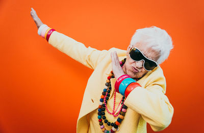 Portrait of stylish senior woman wearing colorful jewelry dancing against orange background