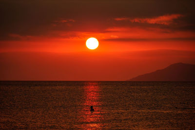 Scenic view of sea against orange sky and silhouette of island