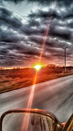 Road passing through landscape against cloudy sky at sunset