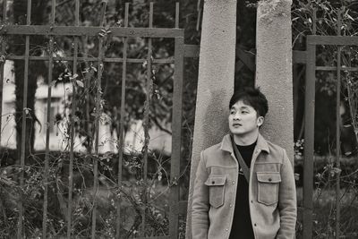 Man looking away while standing by fence