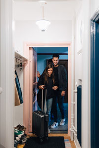 Full length of young friends standing in doorway with luggage