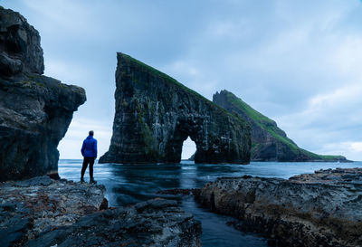 Man standing on rock by sea against sky