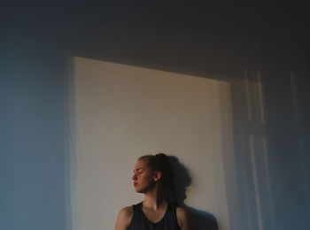 Portrait of beautiful young woman standing against wall at home