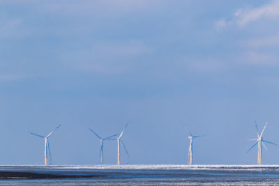 Windmills by sea against sky