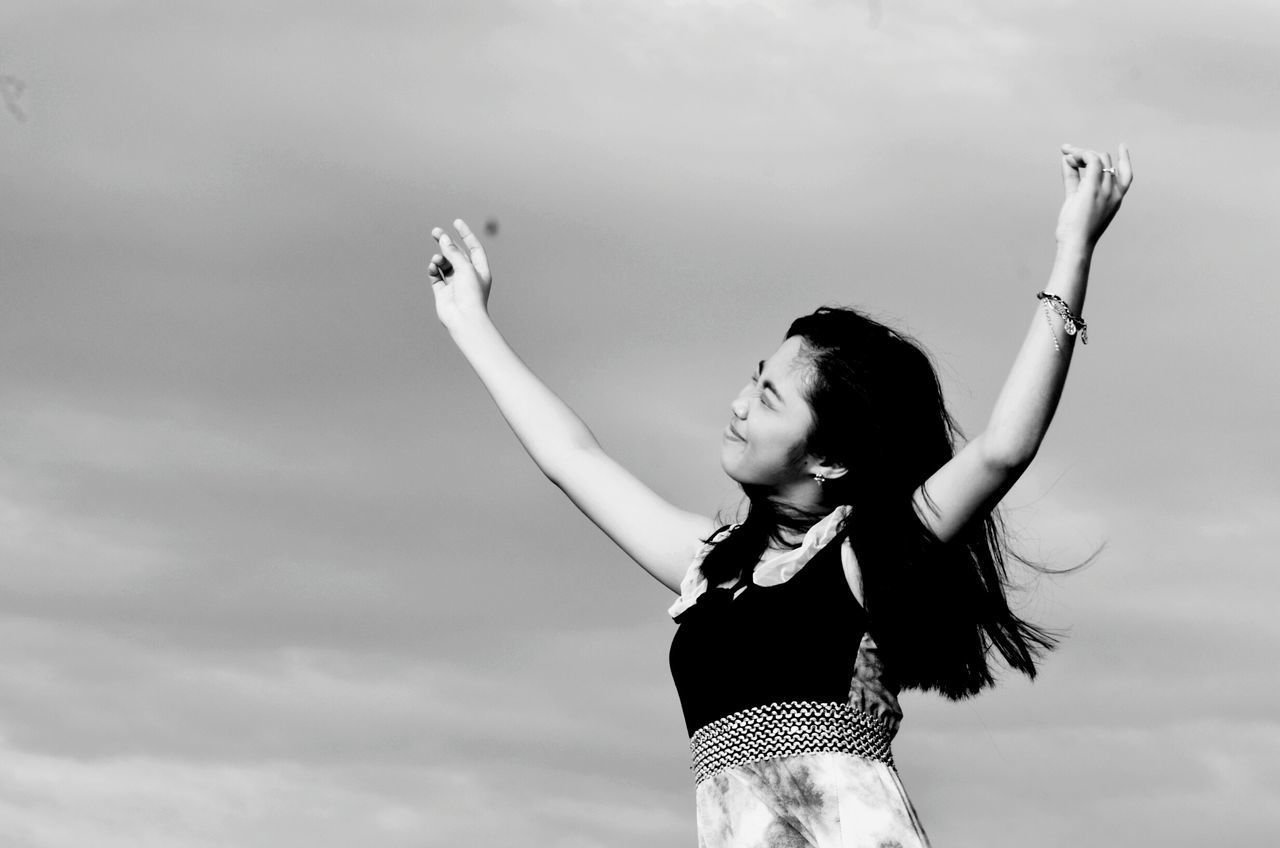 lifestyles, leisure activity, young adult, person, sky, young women, standing, three quarter length, casual clothing, arms raised, low angle view, full length, cloud - sky, arms outstretched, happiness, long hair, fun, girls