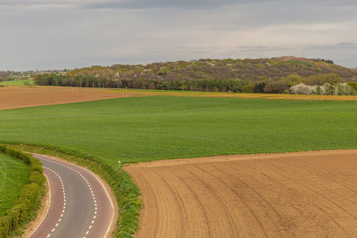 Aerial scenic view of a country road and agricultural field against sky, cultivated and uncultivated