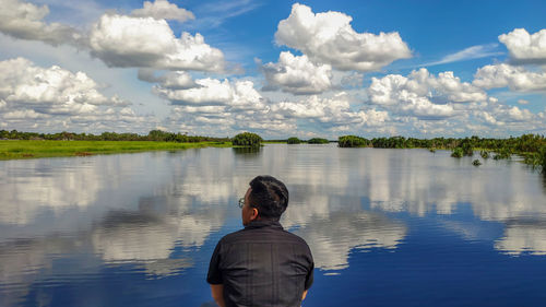 Rear view of man looking at lake against cloudy sky