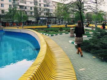 Rear view of woman walking by pond in park against building