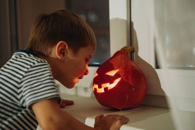 Little boy looking at self made e traditional jack lantern. candle lame reflection on his face