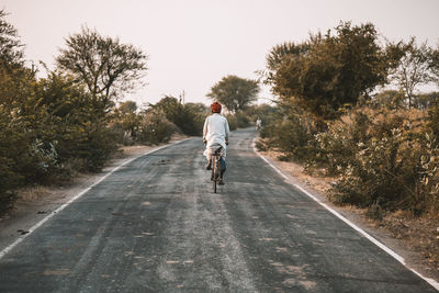 Rear view of man riding motorcycle on road against sky