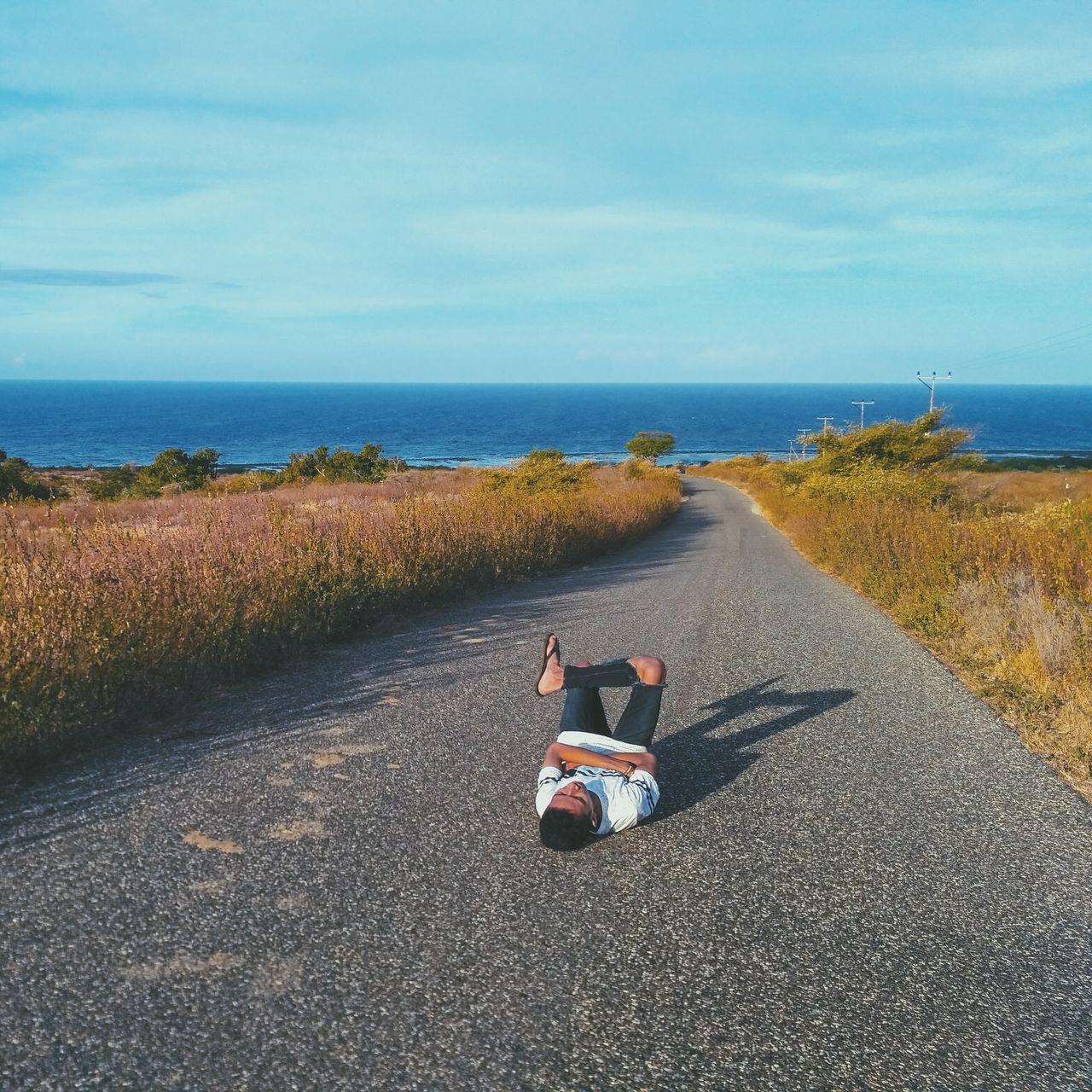 REAR VIEW OF MEN SITTING ON ROAD BY SEA