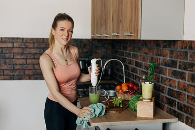 Sportswoman preparing vegan smoothie with green vegetables and celery in the kitchen