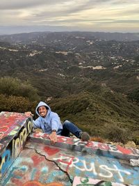 Portrait of man sitting on mountain against sky