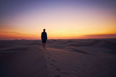 Man on sand dune in desert against sky during sunset
