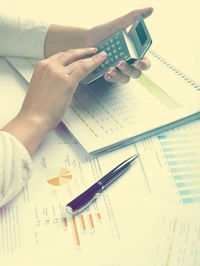 Cropped hands of businesswoman using calculator with documents at desk