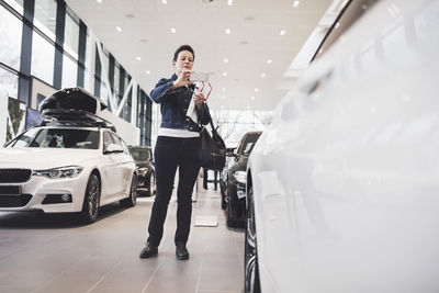 Senior woman photographing new car through mobile phone at showroom