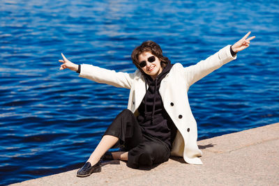 Caucasian brunette with short hair sits on granite curb city. in white coat