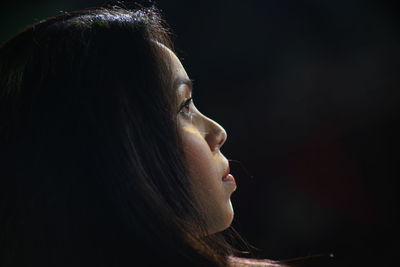 Close-up of woman looking away against black background