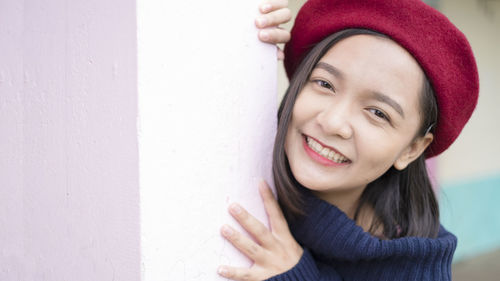 Portrait of smiling young woman standing against wall