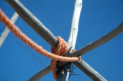 Low angle view of rope tied on pole against blue sky