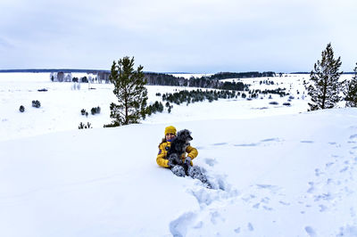 Young cheerful woman sitting in snow holding fluffy gray dog. walking, winter hike, pet love