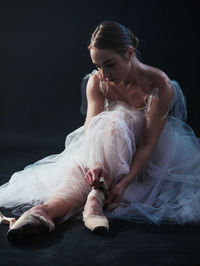 Ballet dancer wearing shoes while sitting against black background