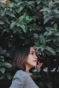 Side view of mid adult woman looking away while standing by plants in park