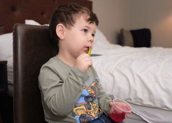 Cute expressive young boy is eating a gelatin snack while watcching tv in a hotel room