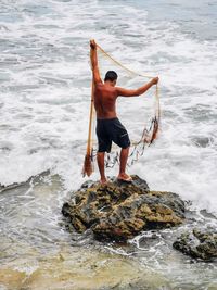 Rear view of man standing on rock in sea