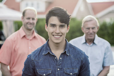 Portrait of confident young man with grandfather and father standing in yard