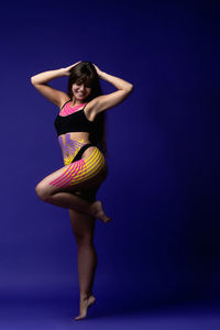 Full length of young woman wearing lingerie while sitting against blue background