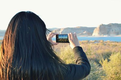 Rear view of woman photographing lake through smart phone